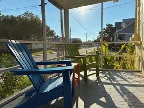 A porch with two chairs and a table, overlooking a street with houses and power lines.