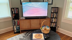 Een woonkamer met een televisie, boekenkasten, een rieten mand en een welkomstbord.