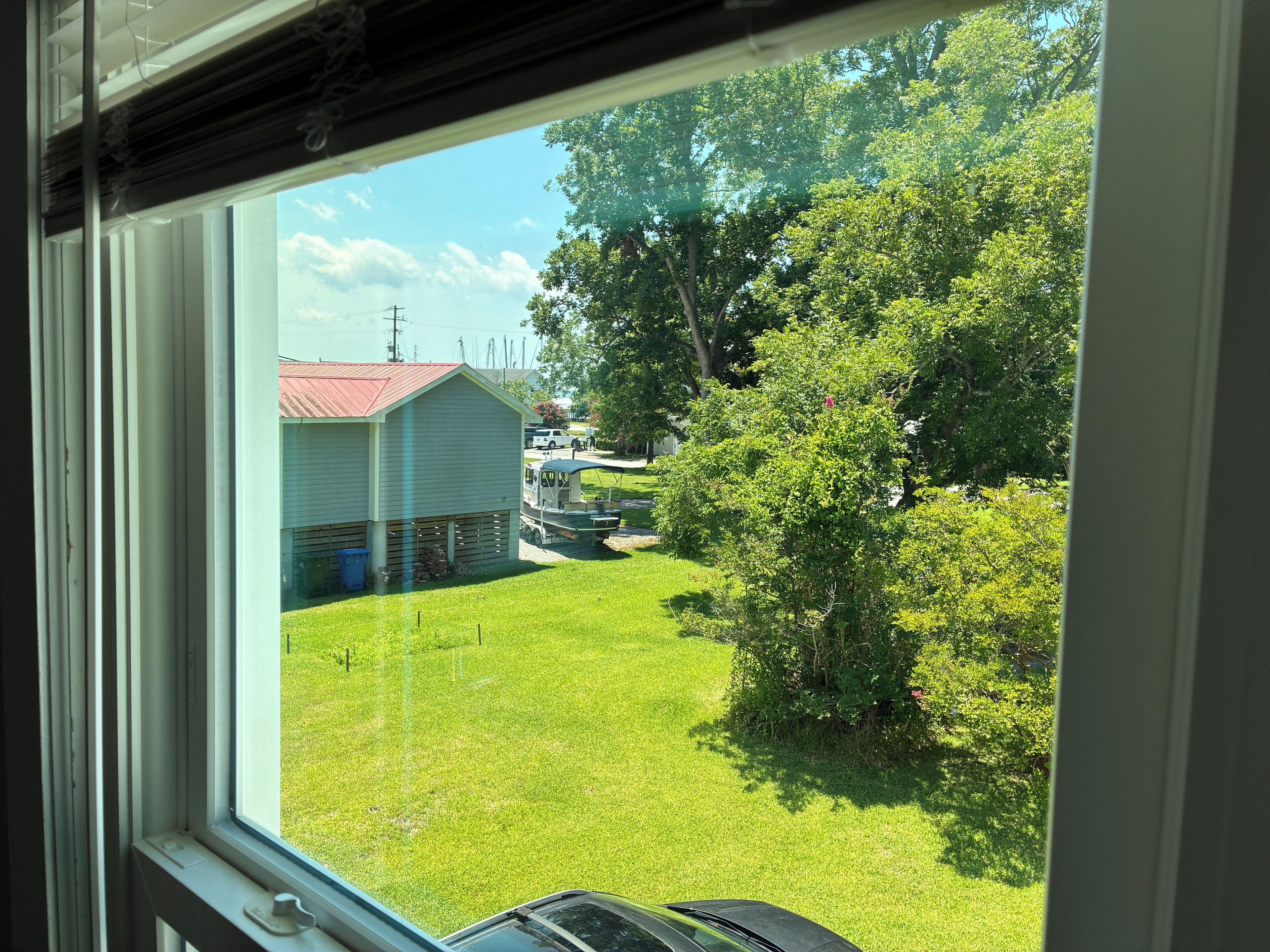 A view through a window of a grassy yard with a house and a parked vehicle.