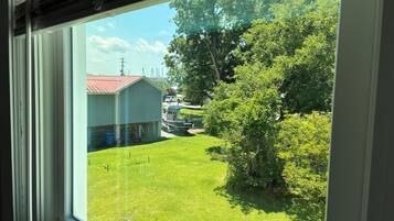 A view through a window of a grassy yard with a house and a parked vehicle.