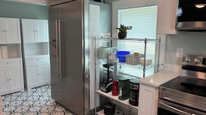 A kitchen with white cabinets, a stainless steel refrigerator, a coffee maker, and a stove. - Screened Porch in Heart of Village, Rotary Car Show on Same Street! (Oriental)