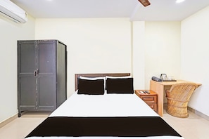 A bedroom with a bed, a wardrobe, a desk with a chair, and a small table with a kettle. - CollectionO Guduvancheri Railway Station (Chengalpattu)