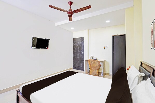 Una habitación de hotel con una cama, un ventilador de techo, una mesita con una tetera y una puerta.