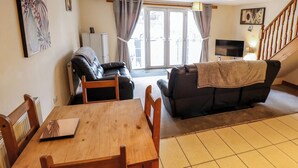 A living room with a wooden dining table, two sofas, a TV, and a staircase. - Holiday Cottage 1 (Skegness)