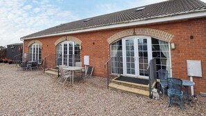A brick building with a tiled roof, a front entrance with a door and windows, and outdoor seating with chairs and a table. - Holiday Cottage 1 (Skegness)