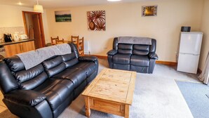 A living room with a black leather sofa, a wooden coffee table, a recliner, and a refrigerator. - Holiday Cottage 1 (Skegness)