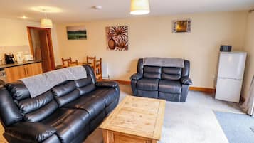 Una sala de estar con un sofá de cuero negro, una mesa de centro de madera, un sillón reclinable y un refrigerador.
