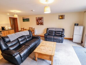 Ein Wohnzimmer mit schwarzem Ledersofa, einem Holztisch, einem Relaxsessel und einem Kühlschrank.