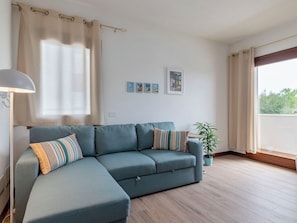 Ein Wohnzimmer mit Ecksofa, einer Lampe, einem Topfpflanzen und einem Fenster mit Vorhängen.
