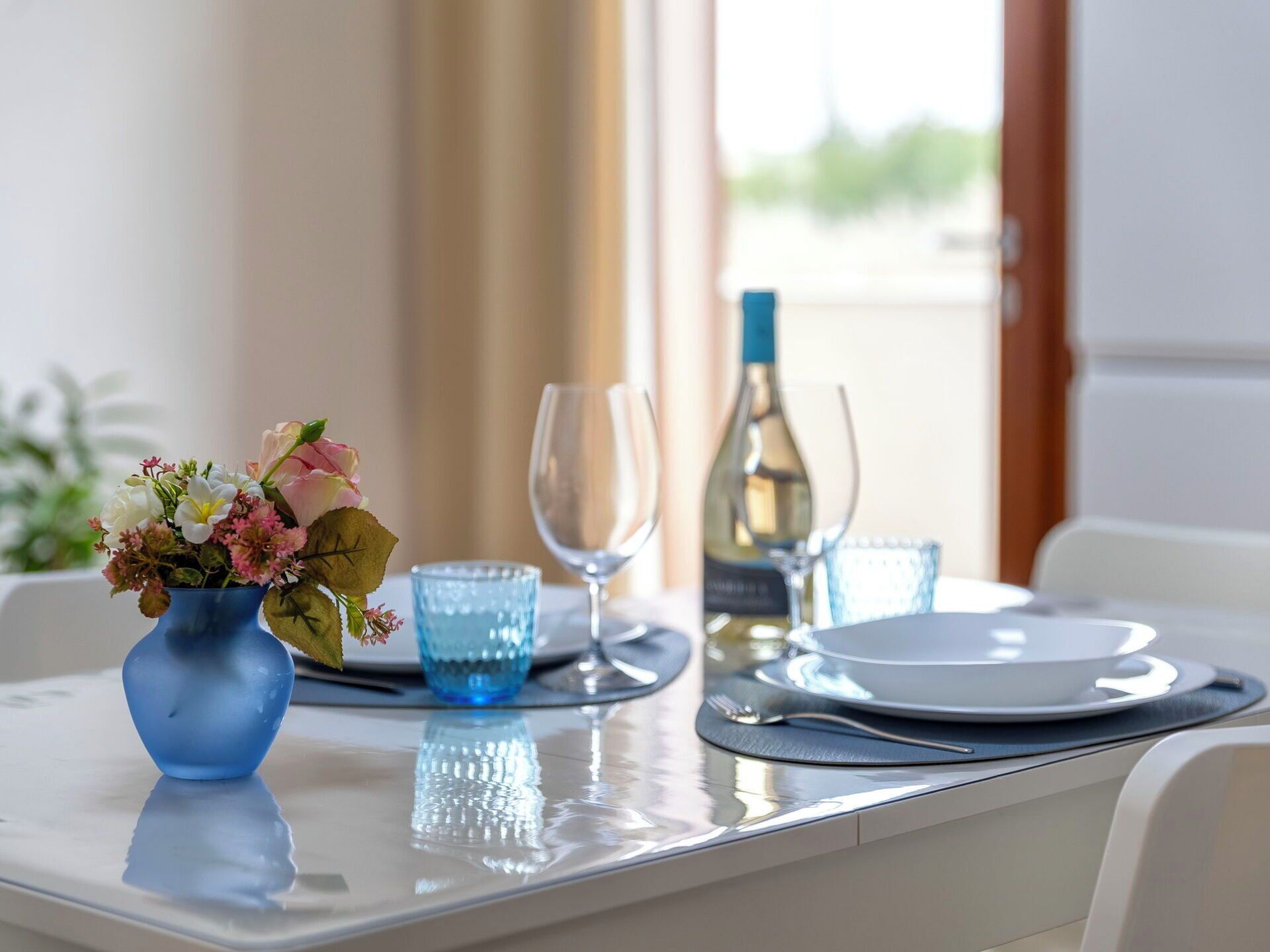 Une table à manger dressée avec un vase de fleurs, deux verres à vin et une bouteille de vin.