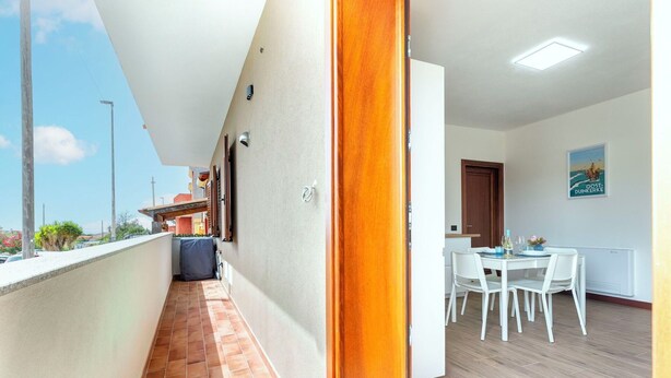Un couloir au sol carrelé mène à un espace repas comprenant une table et des chaises.