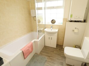 A bathroom with a bathtub, sink, toilet, and a window providing natural light. - Holiday Cottage 3 (Skegness)