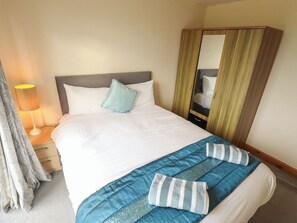 A neatly made bed with a pillow, a bedside lamp, and a mirror cabinet. - Holiday Cottage 3 (Skegness)