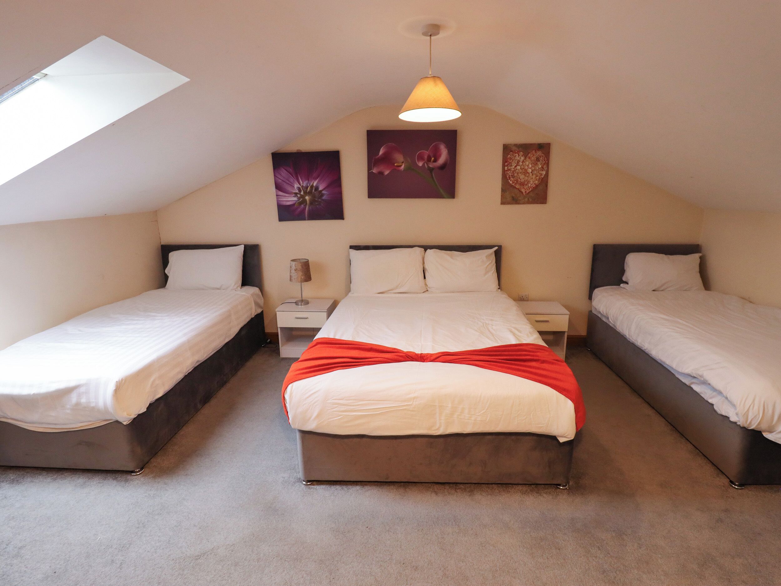 A bedroom with two single beds, a larger bed, and a nightstand with a lamp.