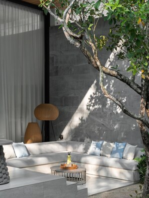A modern outdoor seating area with a sofa, a round table with a glass top, and a decorative lamp. - Layan - 10 Min to Beach - Private Designer Villa (Thep Krasatti)