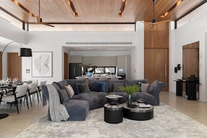 A modern living room with a sectional sofa, a coffee table, and a dining area with chairs and a table set for a meal. - Layan - 10 Min to Beach - Private Designer Villa (Thep Krasatti)