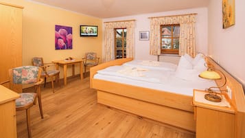 Een hotelkamer met een houten bed, een bureau, twee stoelen, een televisie en een raam met gordijnen.