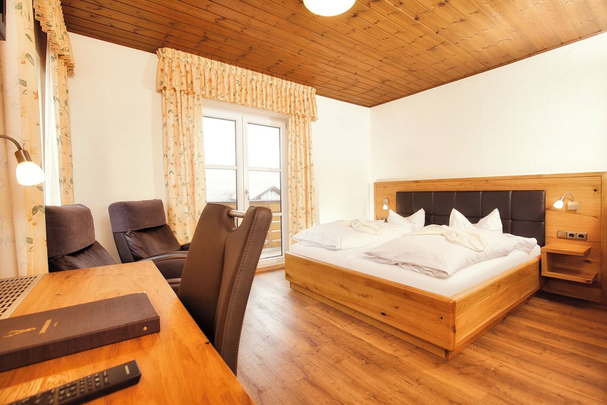 A hotel room with a wooden ceiling, a bed with white bedding, a desk with a laptop, and two chairs.