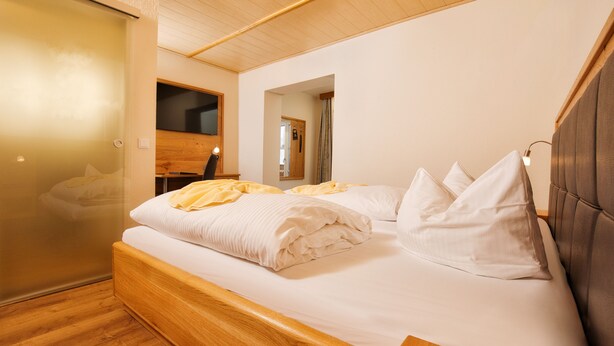 Ein Schlafzimmer mit einem hölzernen Bett, weißer Bettwäsche, einem Spiegel und einer Holzbalkendecke.