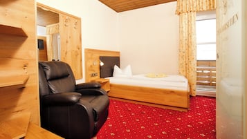 A hotel room with a wooden headboard, a leather chair, a bed with white bedding, and a red carpet.