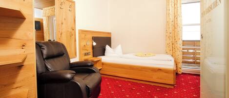 Habitación de hotel con cabecera de madera, una silla de cuero, cama con ropa blanca y alfombra roja.