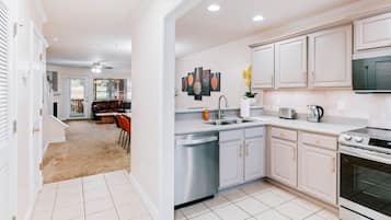 A modern kitchen with white cabinetry, stainless steel appliances, and a tiled floor.