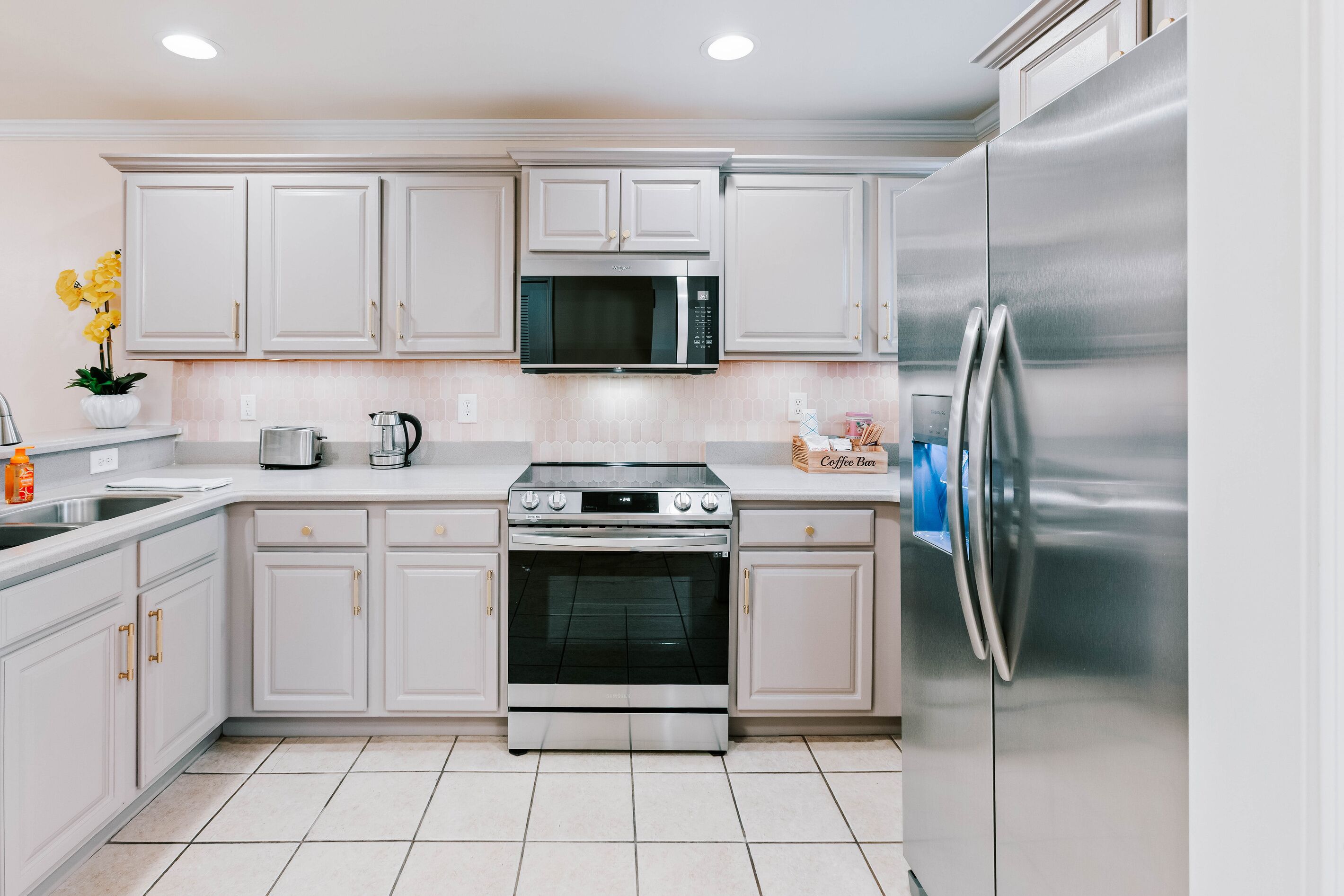 A modern kitchen with white cabinetry, stainless steel appliances, and a tiled floor.
