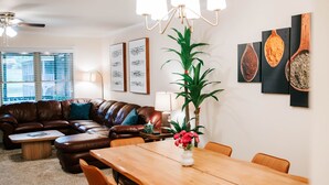 Ein modernes Wohnzimmer mit einem braunen Ledersofa, einem Holzesstisch mit Stühlen, einer Topfpflanze und Bildern an den Wänden.