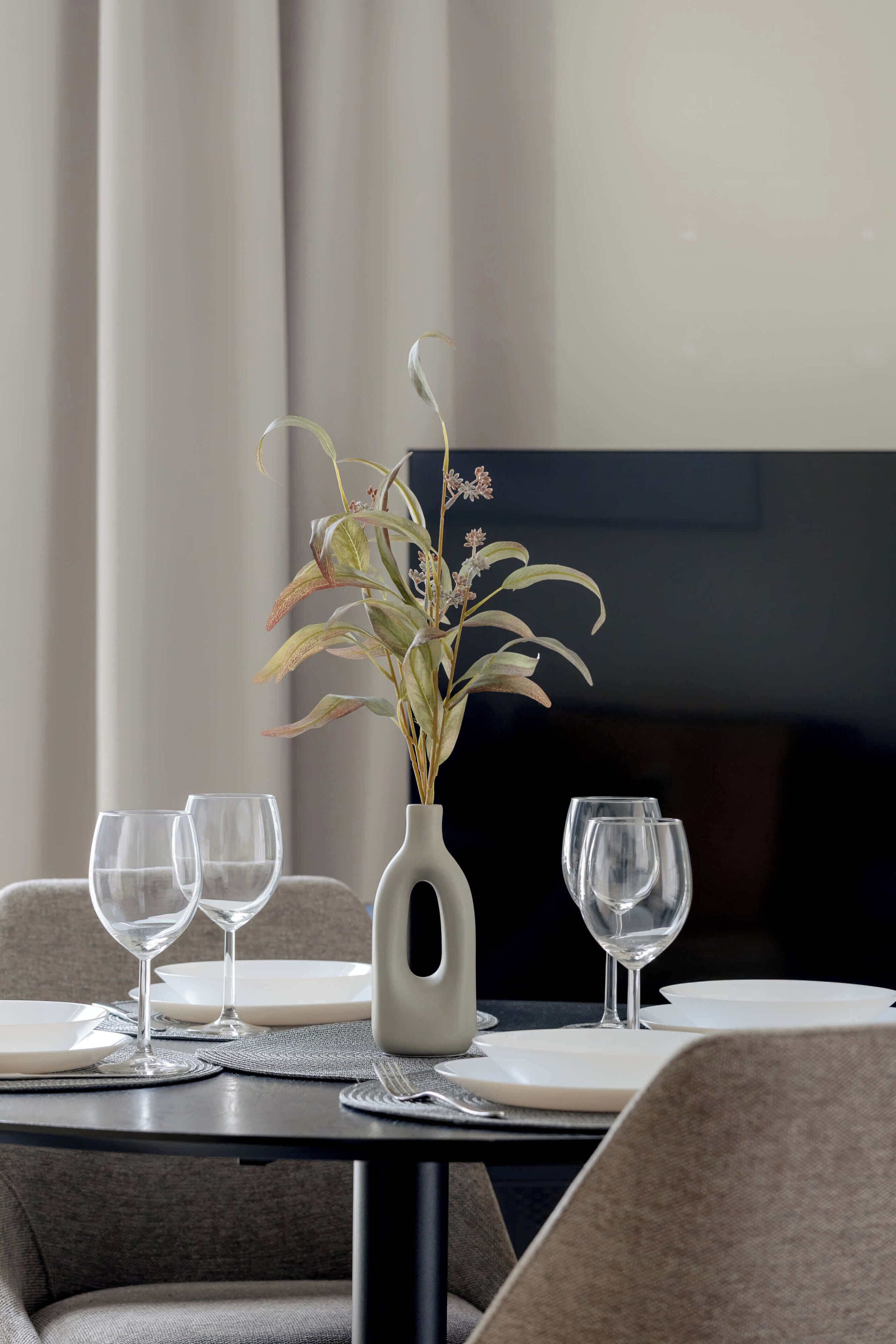 Ett matbord med en vas med blommor, två tomma vinglas och en tv i bakgrunden.