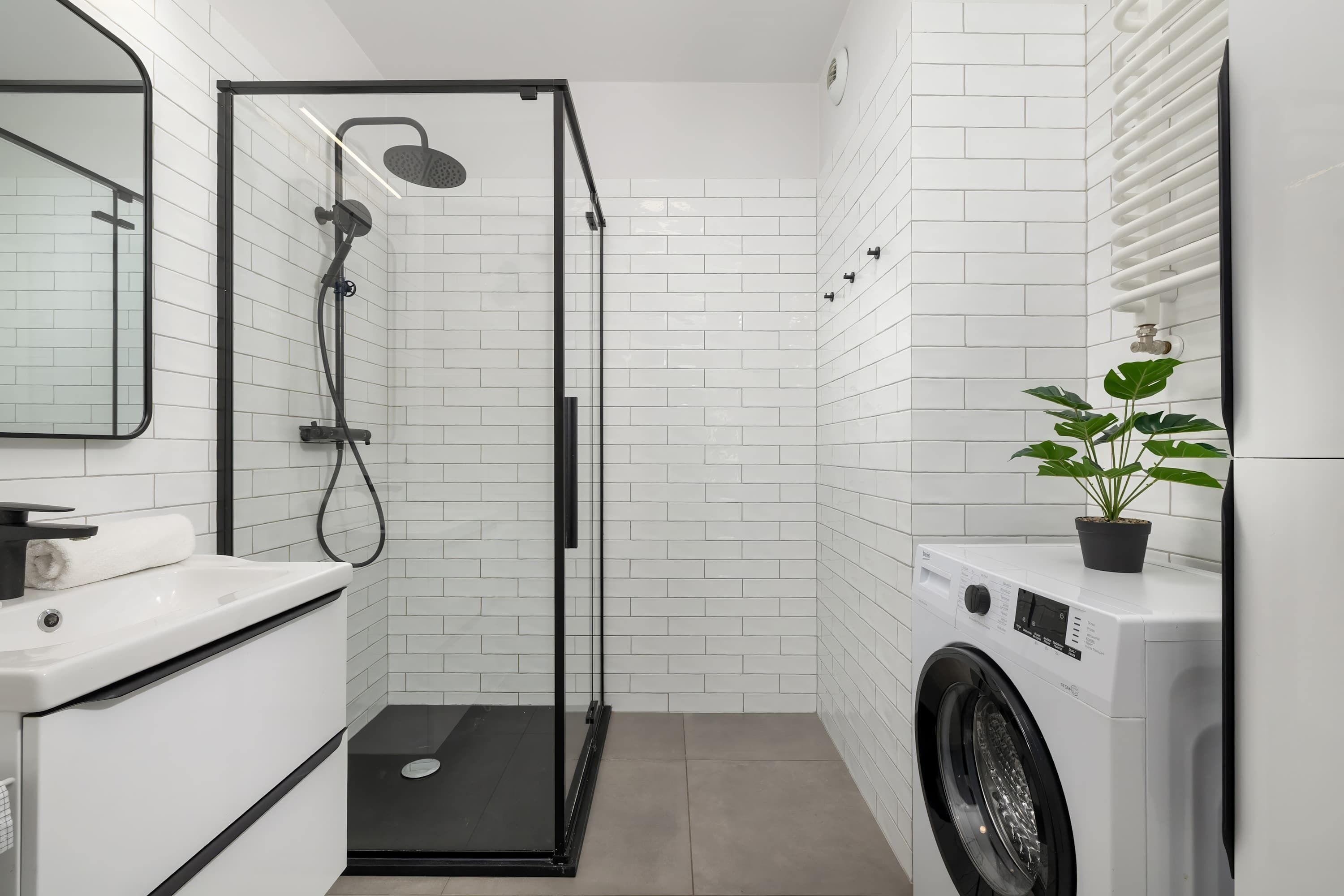 Une salle de bain compacte comprenant une douche, un lavabo et un lave-linge.