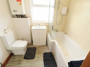 A bathroom with a toilet, sink, shower, and a window. - Holiday Cottage 2 (Skegness)