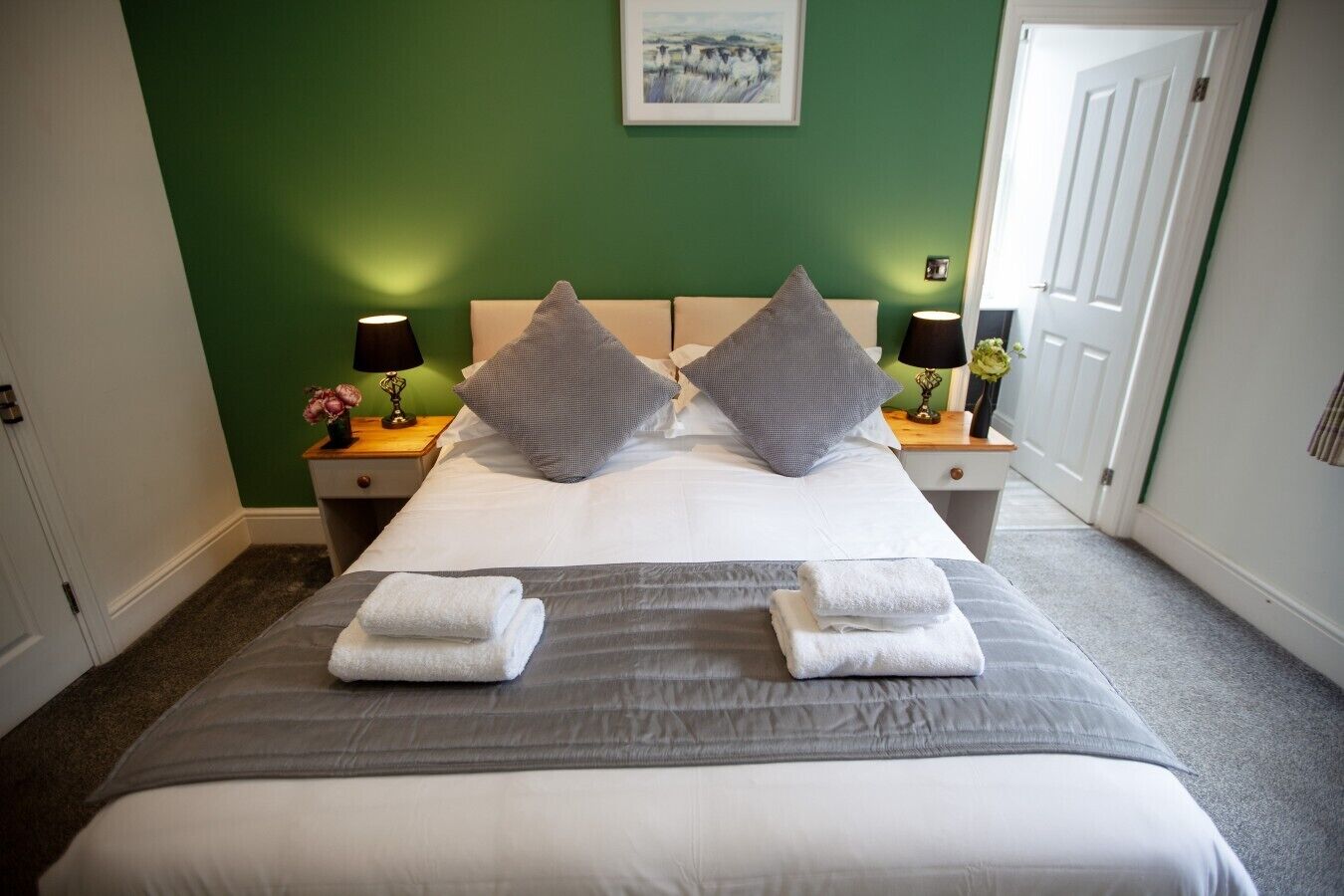 A neatly made bed with two pillows, a bedside table with a lamp, and a framed picture on the wall.