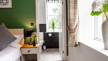 A bedroom with a bed, bedside table, lamp, and a window with a curtain.