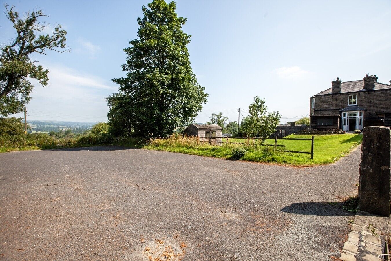 A rural road leading to a stone house with a grassy yard and a small wooden structure.