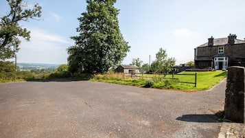 A rural road leading to a stone house with a grassy yard and a small wooden structure.
