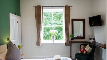 A hotel room with a bed, a desk, a chair, a window with curtains, and a flat-screen TV.