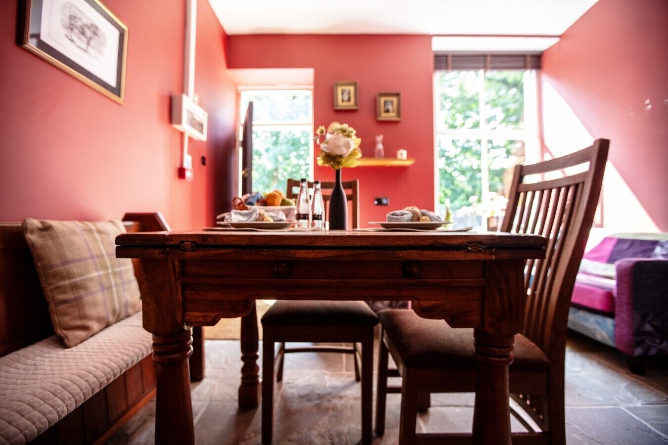 A dining area with a wooden table, chairs, a bench, and a vase with flowers.