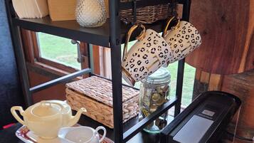 Un área de cocina con cafetera, tetera, tazas y un estante con utensilios y un tarro.