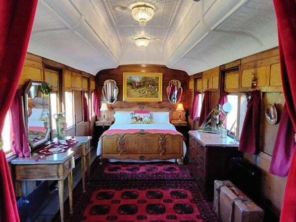 A traditional room with a large bed, wooden walls, a chandelier, and a painting above the bed.