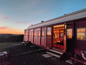 A stationary train car with an open door, a set of stairs leading up to the entrance, and a view of the surrounding landscape.