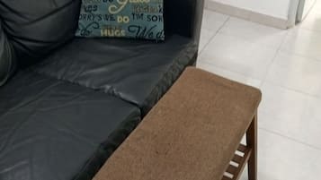 Ein Wohnzimmer mit einem schwarzen Ledersofa, einer braunen Bank und einem an der Wand befestigten Schrank.