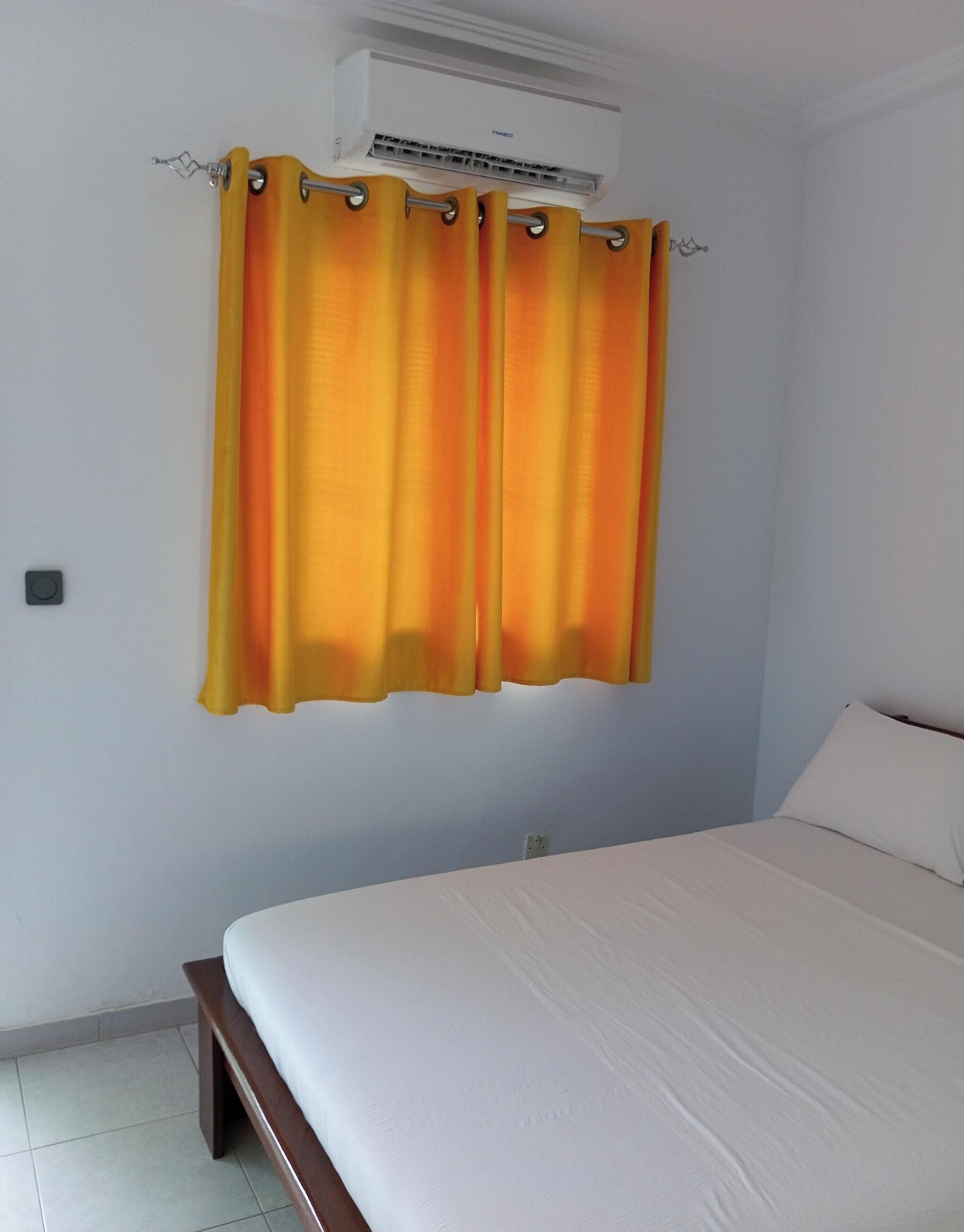 Un dormitorio con una cama, una cortina y un equipo de aire acondicionado en la pared.