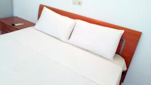 A bed with a wooden headboard, a white mattress, and two pillows. - RESIDENCE BELLE VUE PALMERAIE (ABIDJAN)
