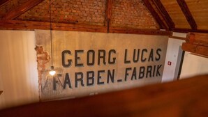 A sign with the name 'GEORG LUCAS FARBEN-FABRIK' in a room with exposed brick walls and wooden beams. - Alter Hafen Marktsteft (Marktsteft)