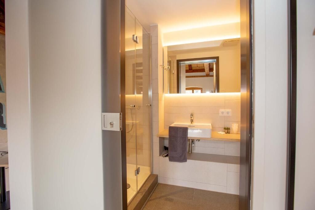 Ein modernes Badezimmer mit einer Duschkabine aus Glas, einem weißen Waschbecken und einem Spiegel darüber.