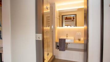Ein modernes Badezimmer mit einer Duschkabine aus Glas, einem weißen Waschbecken und einem Spiegel darüber.