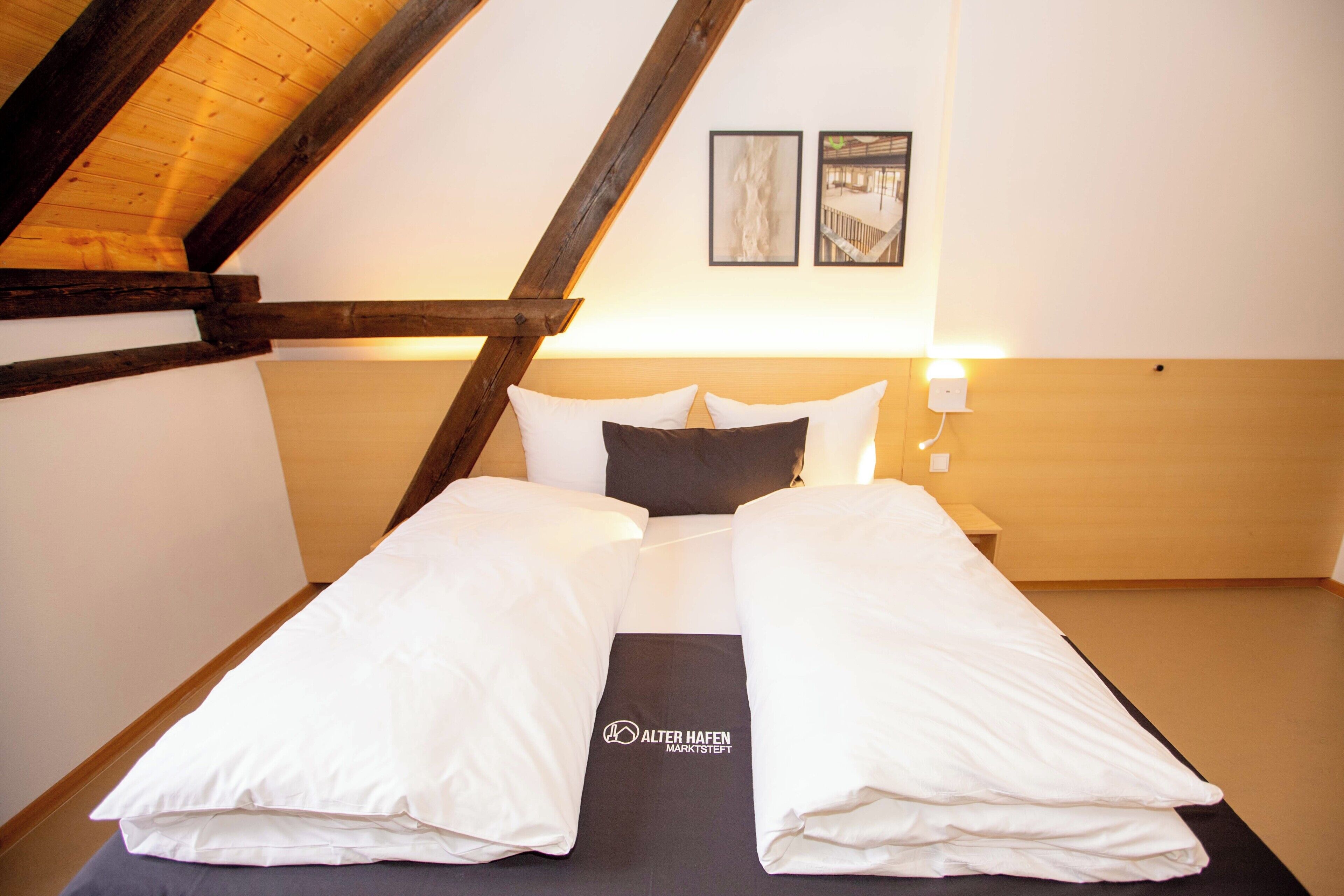 A hotel room with a high ceiling, wooden beams, a bed with white linens, and two framed pictures on the wall.