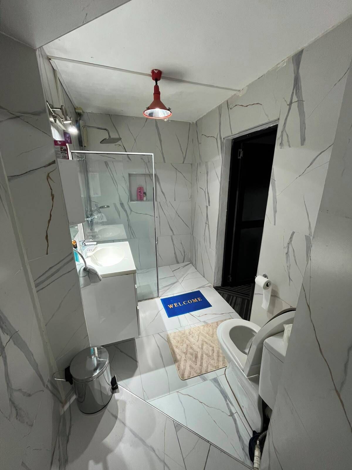 Une salle de bain moderne avec un sol en marbre, une douche en verre, un lavabo blanc et un luminaire rouge au plafond.