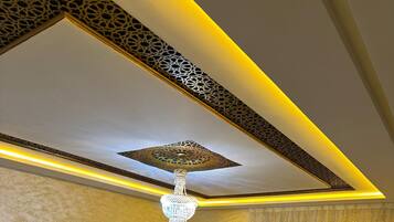 Une pièce avec un canapé d’angle, un lustre, un plafond décoré et une fenêtre avec des rideaux.