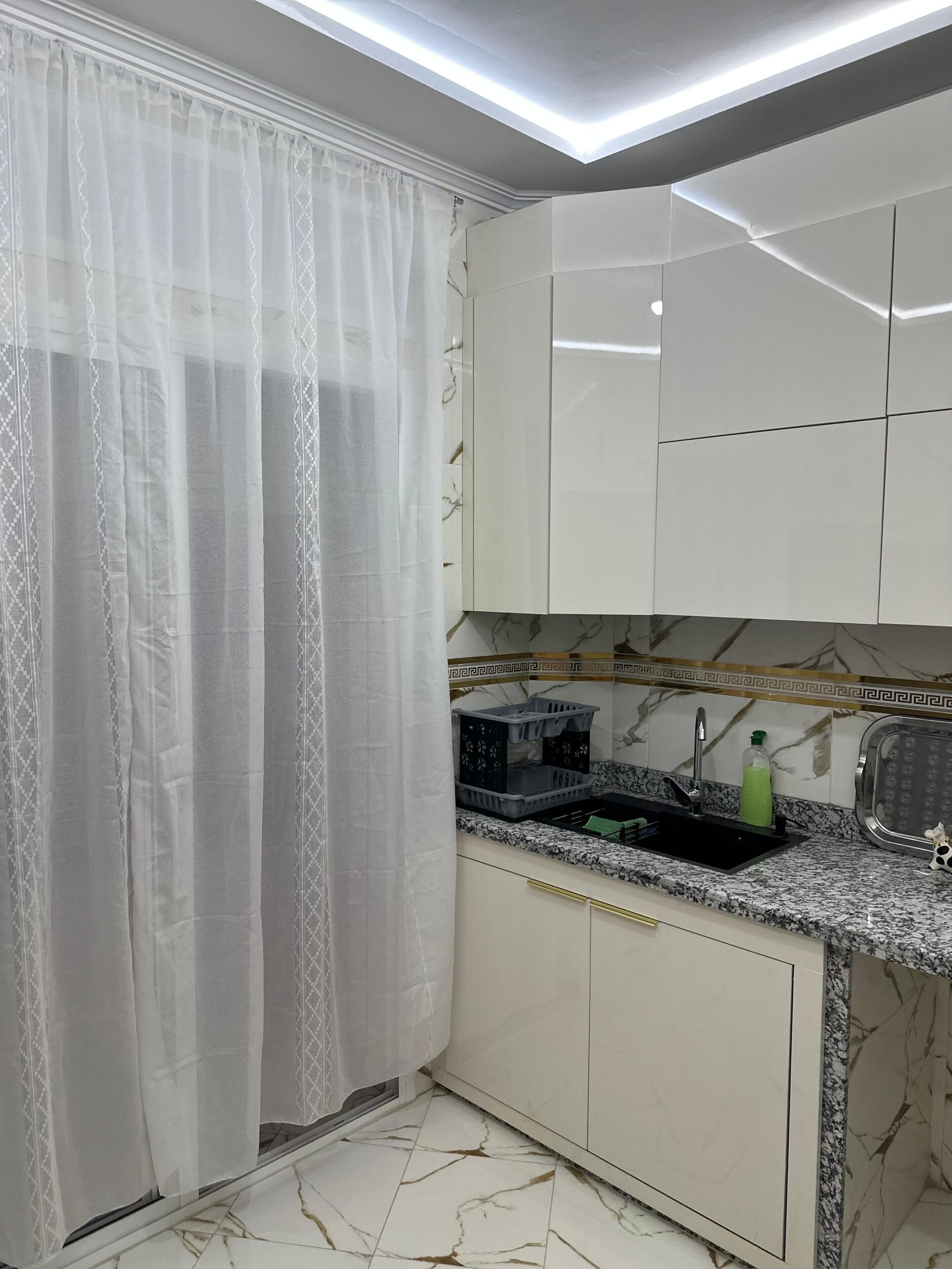 A kitchen with a marble floor, white cabinets, a black countertop, and a green bottle.